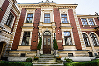 Obraz przedstawia front budyneku Instytutu Pedagogiki UJ przy ul. Batorego 12, jest to: wejście główne ze schodami, okna i ozdobny gzyms; budynek jest z czerwonej cegły.